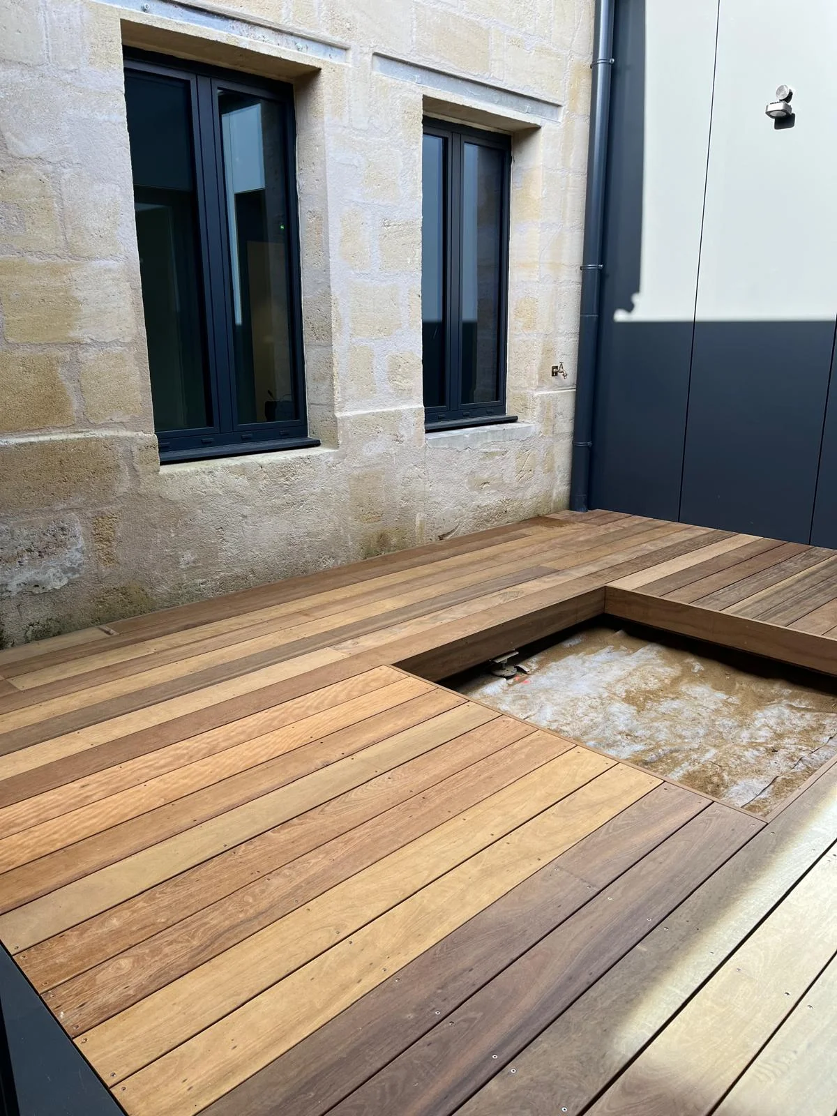 Aménagement d'un patio avec une terrasse bois et massif pour plantations réalisé par Mea créations